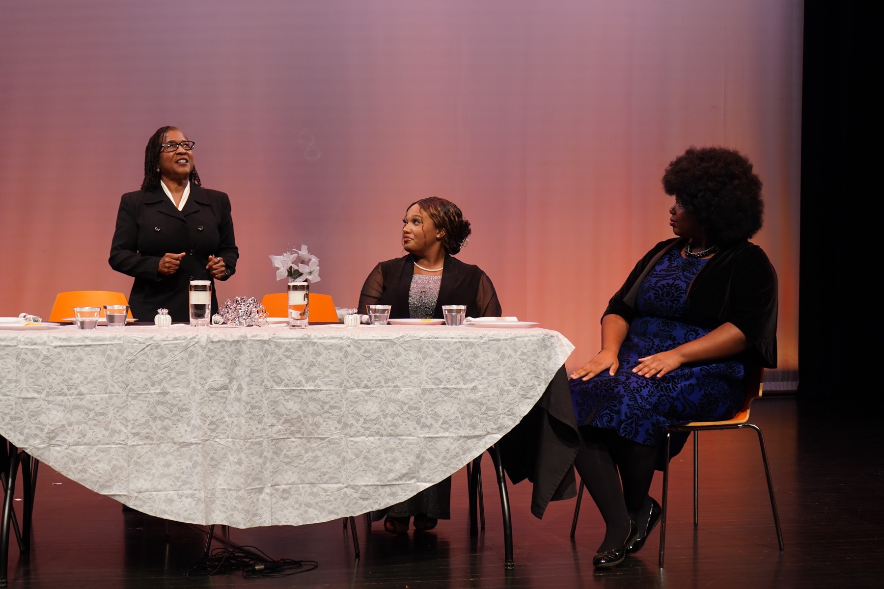 Leslie and two cast members gathered around a table under warm stage lighting in When the Truth Comes Out
